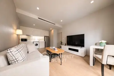 Modern living room with open kitchen, stylish furniture, and large TV in a cozy apartment.