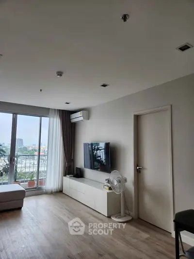 Modern living room with large window and city view, featuring sleek furniture and neutral tones.