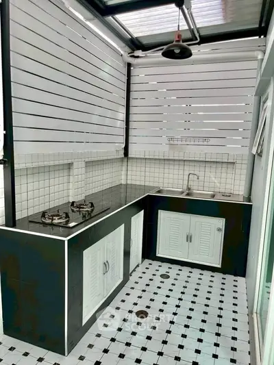 Modern outdoor kitchen with sleek black and white design, featuring gas stove and tiled backsplash.