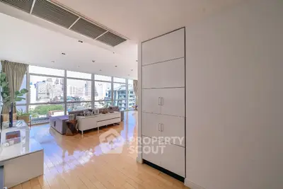 Spacious modern living room with large windows and city view, featuring sleek wooden flooring and contemporary furniture.