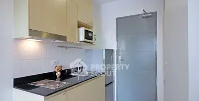 Modern compact kitchen with sleek cabinets and built-in microwave in a cozy apartment.