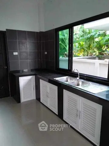 Modern kitchen with sleek black countertops and large window overlooking lush greenery.