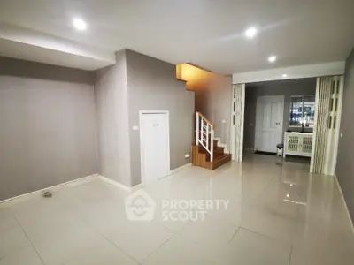 Spacious and modern living area with glossy tiled floors, recessed lighting, and a warm wooden staircase leading to an inviting kitchen.