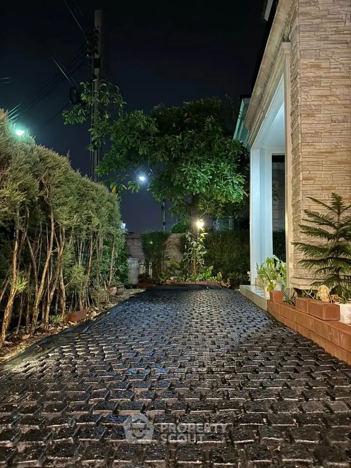Charming night view of a garden pathway leading to a modern home entrance, surrounded by lush greenery.