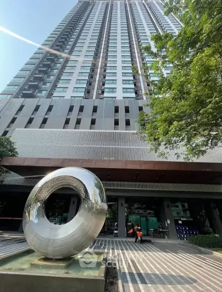 Modern high-rise building with unique sculpture at entrance, showcasing urban architectural elegance.