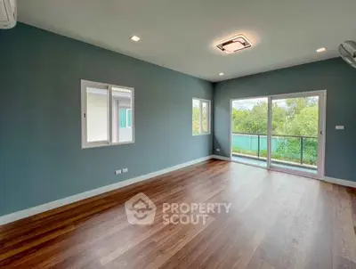 Spacious empty living room with large windows and wooden flooring, offering a serene view of greenery.