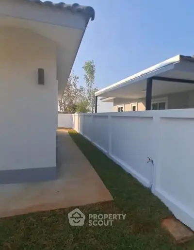 Modern exterior view of a single-story home with white walls and a neatly landscaped yard.