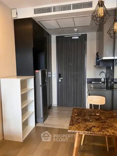 Modern kitchen with sleek cabinetry, marble table, and compact fridge in a stylish apartment.