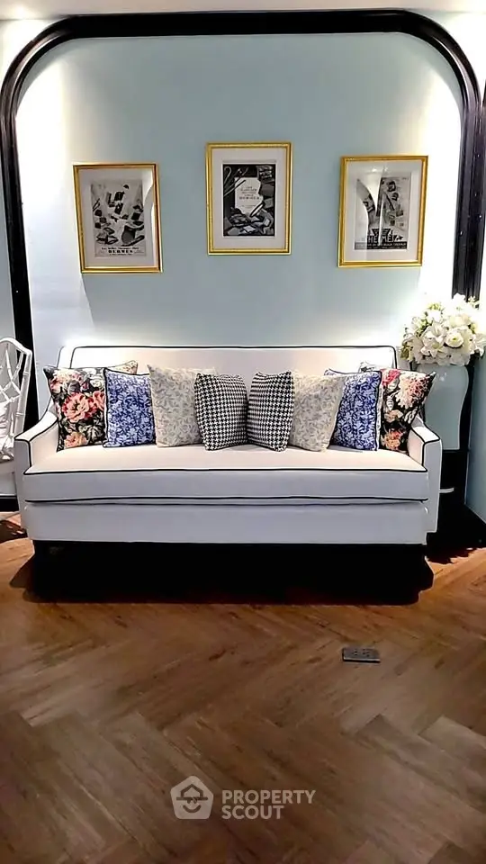 Elegant living room with stylish sofa and decorative pillows, framed art on pastel walls.