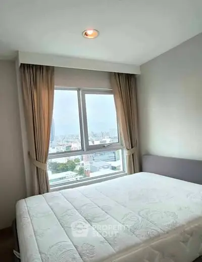 Cozy bedroom with city view, featuring large window and elegant curtains.