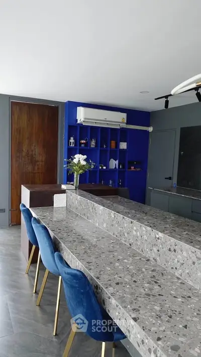 Modern kitchen with terrazzo countertops and blue chairs, featuring a sleek open layout and stylish decor.