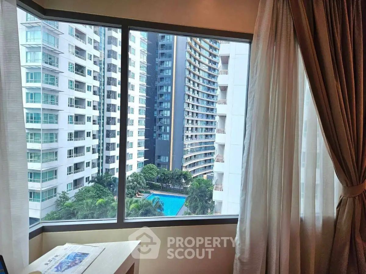Stunning high-rise view from a modern apartment window overlooking a pool and cityscape.