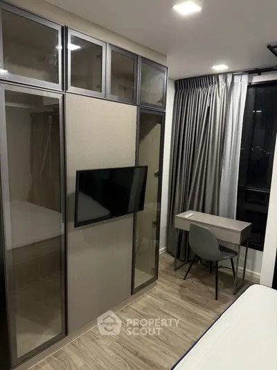Modern bedroom with sleek wardrobe, wall-mounted TV, and compact study desk.