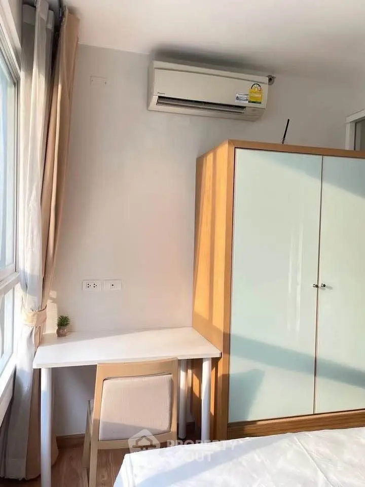 Cozy bedroom corner with desk, chair, wardrobe, and air conditioning in bright natural light.