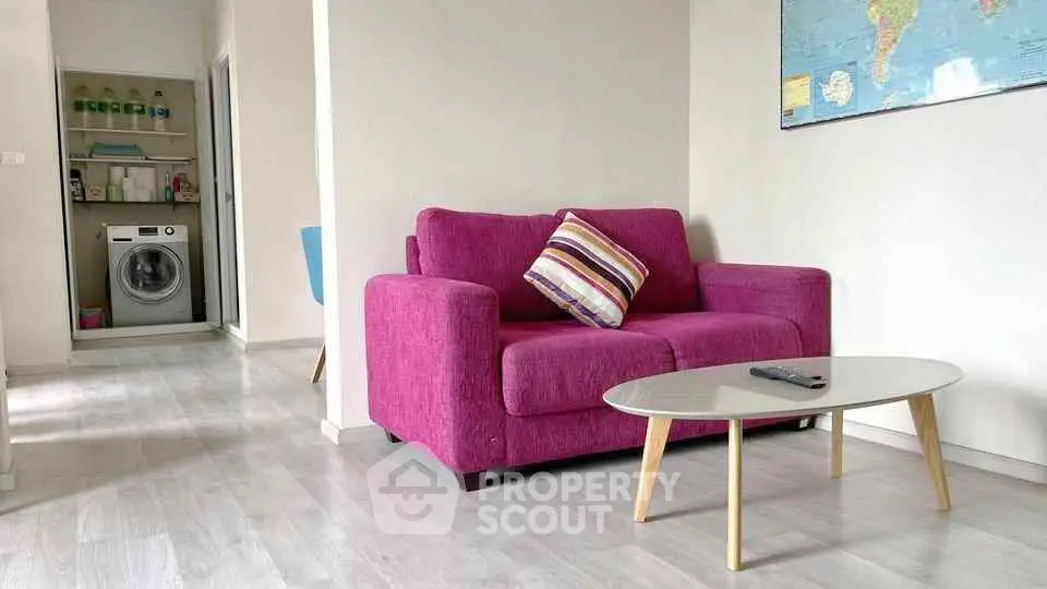 Modern living room with vibrant pink sofa and sleek coffee table, featuring a washing machine in the background.