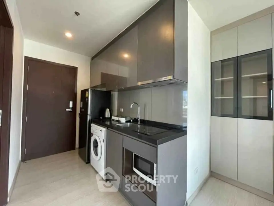 Modern kitchen with sleek cabinets, washing machine, and microwave in compact layout.