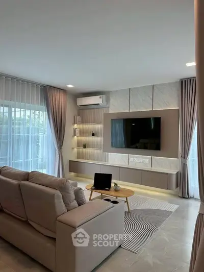 Modern living room with stylish decor, large TV, and natural light through sheer curtains.