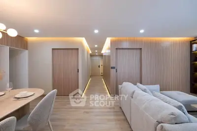 Modern living room with cozy seating and elegant dining area, featuring warm lighting and sleek wooden accents.