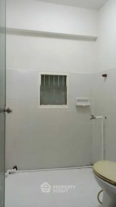 Minimalist bathroom with white tiles and small window, ideal for compact spaces.