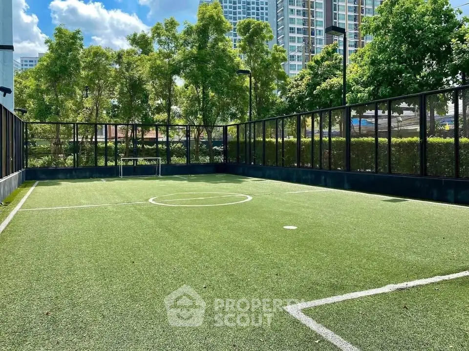 Modern outdoor soccer field in a residential complex with lush greenery and cityscape views.
