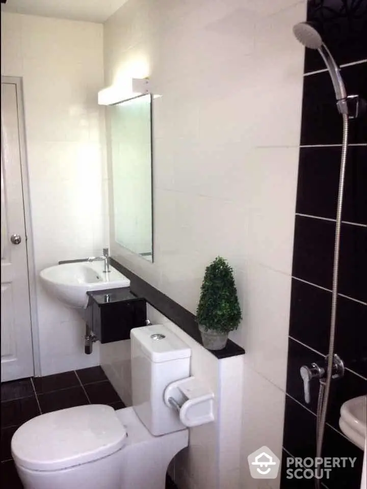 Sleek modern bathroom with contrasting black and white tiles, well-lit mirror, and a refreshing shower area, perfect for contemporary living.