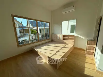Bright bedroom with large window and wooden flooring, featuring a modern bed frame and air conditioning.