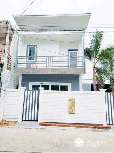 Modern two-story house with balcony and gated entrance, featuring sleek design and palm tree landscaping.