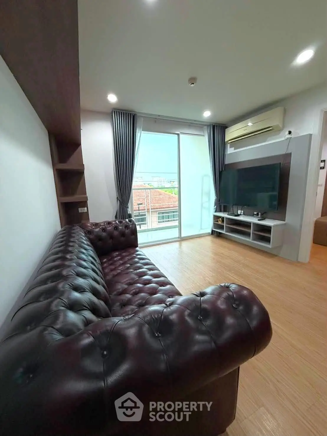 Modern living room with leather sofa and large TV, featuring floor-to-ceiling windows and wooden flooring.