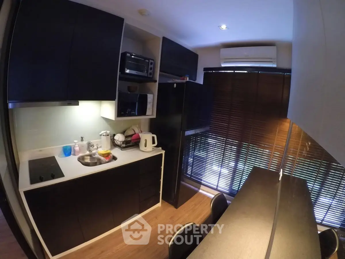 Modern kitchen with sleek black cabinets and dining area, featuring natural light and contemporary appliances.