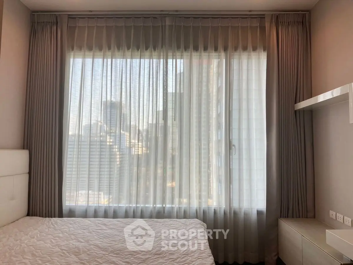 Modern bedroom with large window offering city view, elegant curtains, and minimalist decor.