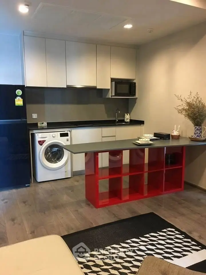 Modern kitchen with washing machine and red shelving unit, sleek design.