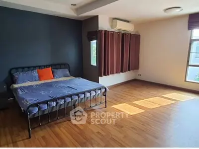 Spacious bedroom with wooden flooring and natural light, featuring a cozy bed and modern decor.