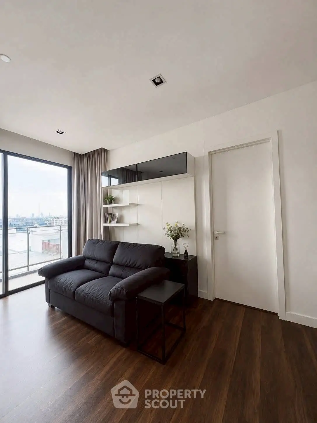 Modern living room with sleek black sofa and large window offering city view