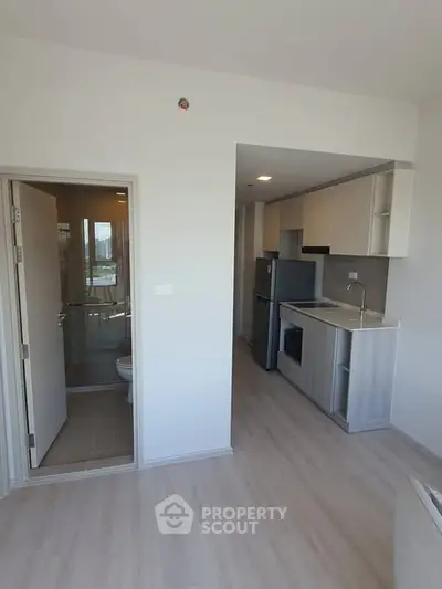 Modern apartment interior with compact kitchen and bathroom, featuring sleek cabinetry and light wood flooring.