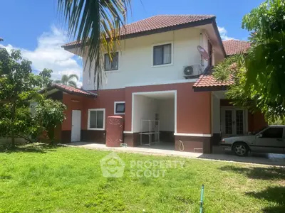 Charming two-story house with red-tiled roof and lush green garden, perfect for family living.