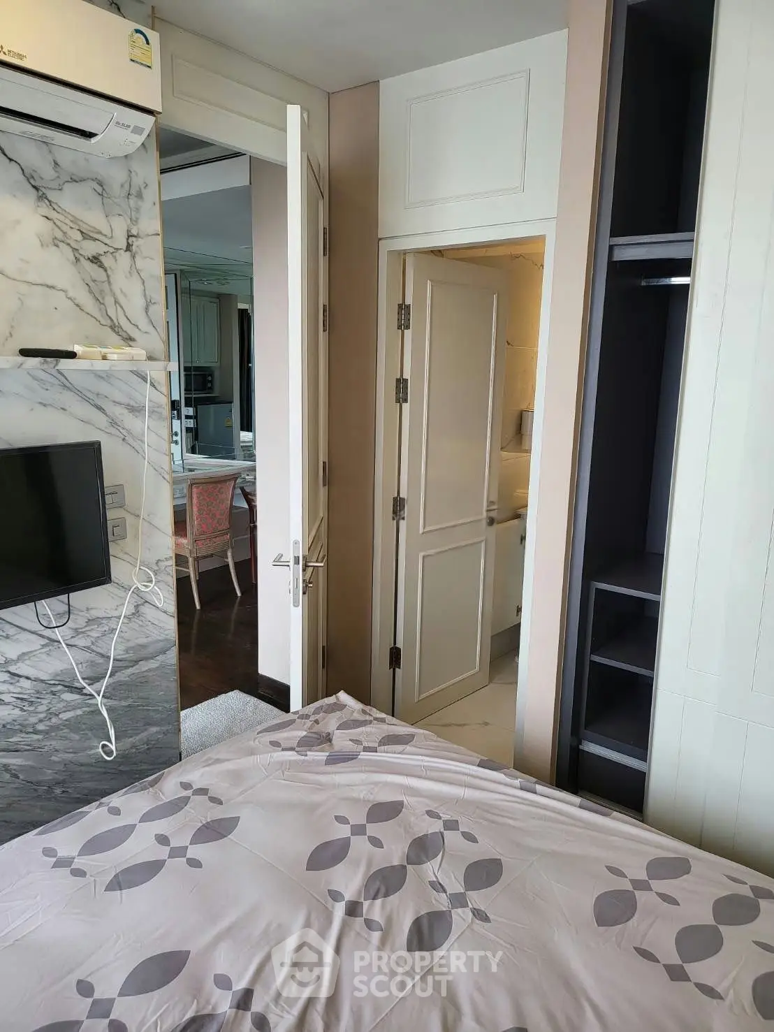 Modern bedroom with marble accent wall and built-in wardrobe, featuring air conditioning and stylish decor.