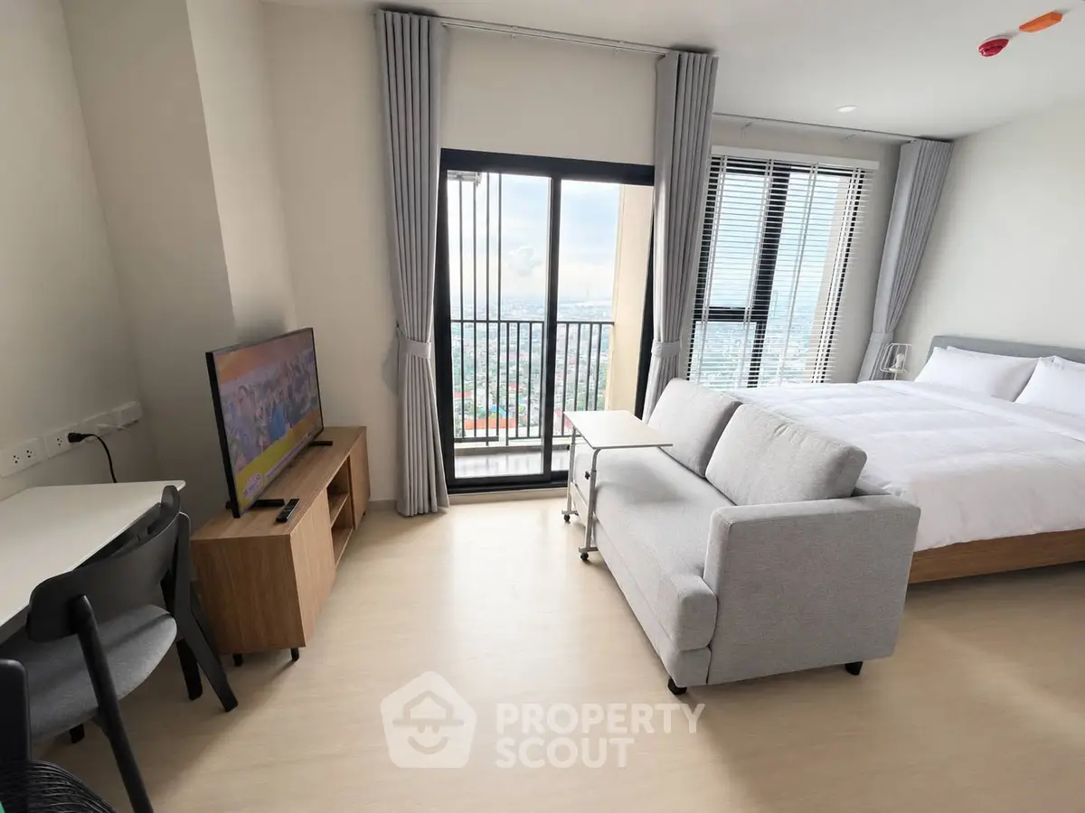 Modern studio apartment with balcony and city view, featuring cozy bed, sofa, and TV setup.