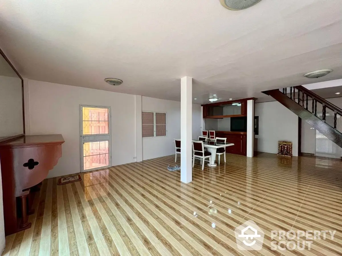 Spacious living area with gleaming hardwood floors, elegant staircase, and abundant natural light, perfect for entertaining and family living.