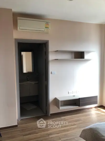 Modern bedroom with air conditioning and wooden flooring, featuring built-in shelves and a glimpse of an ensuite bathroom.