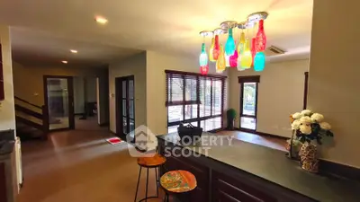 Spacious living area with colorful bottle chandelier and large windows for natural light.
