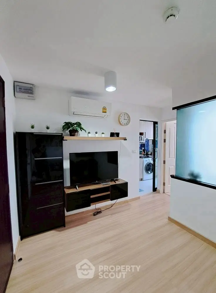Modern living room with sleek black furniture and wall-mounted TV, featuring light wood flooring.