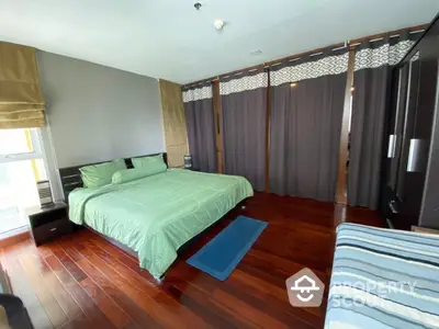 Spacious bedroom with polished hardwood floors, large windows with ample natural light, and elegant dark curtains.