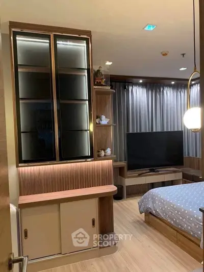 Modern bedroom with stylish wooden furniture and large TV, featuring elegant lighting and floor-to-ceiling curtains.