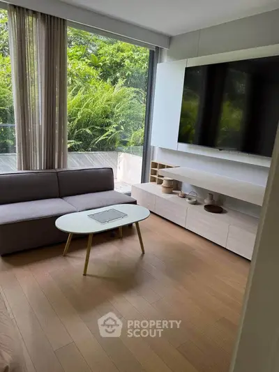 Modern living room with large window and stylish furniture overlooking lush greenery.