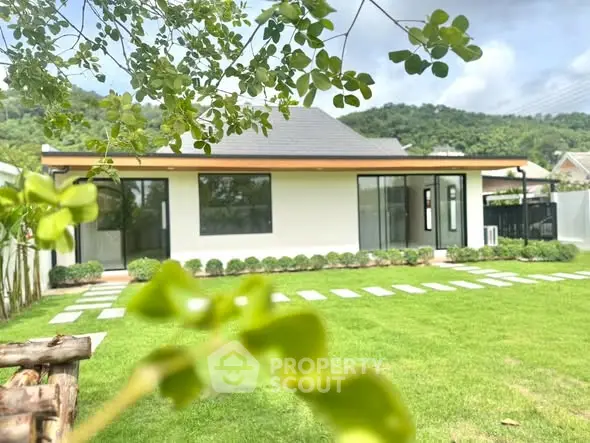 Charming modern house with lush green lawn and scenic mountain backdrop, perfect for serene living.