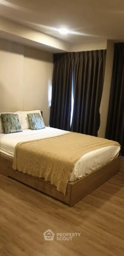 Cozy bedroom with wooden flooring and elegant curtains, perfect for relaxation.