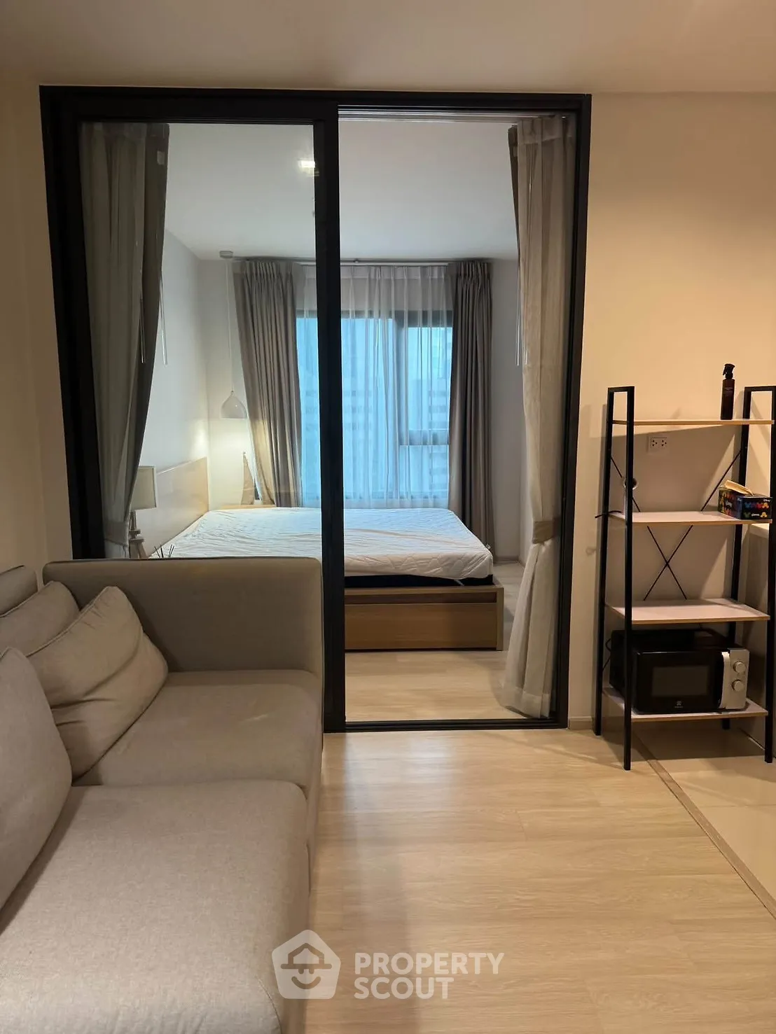 Modern studio apartment with cozy living area and bedroom separated by glass partition.