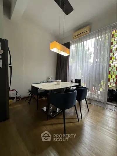 Modern dining area with stylish lighting and large window, featuring sleek furniture and wooden flooring.