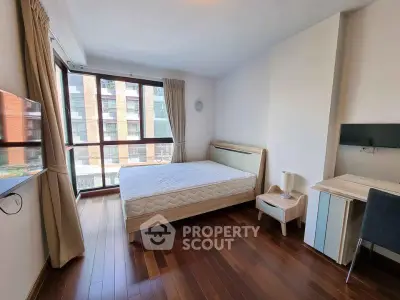 Spacious bedroom with large windows and hardwood floors in modern apartment.