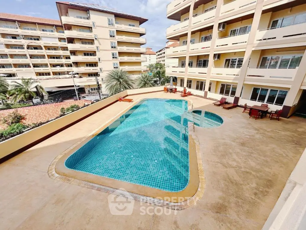 Spacious outdoor pool area in a modern apartment complex with sun loungers and palm trees.